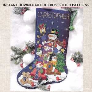 以下が含まれることがあります： 雪だるまの家族と「クリストファー」という名前が刺繍された青いクリスマスストッキング。ストッキングは白い雪玉と松の枝で囲まれています。