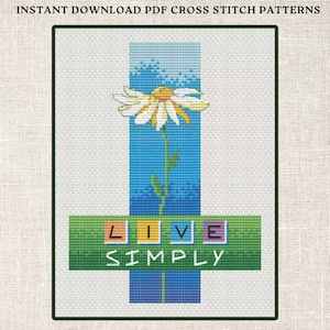 May include: Cross stitch pattern featuring a white daisy with a yellow center, a blue sky background, and the text "LIVE SIMPLY" in colorful letters.