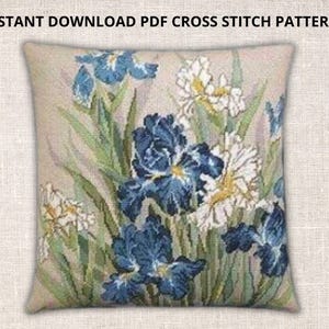 May include: A square pillow with a cross-stitch design featuring blue and white irises with green leaves. The pillow has a beige background. Text at the top reads "INSTANT DOWNLOAD PDF CROSS STITCH PATTERNS."