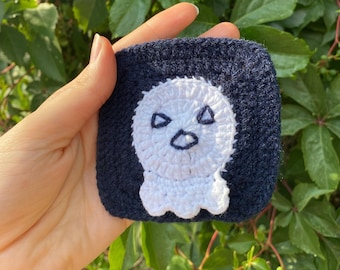 May include: A crocheted ghost with a white face and black eyes on a dark blue background.