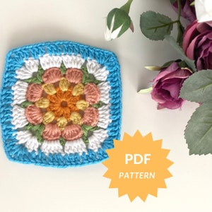 Puede incluir: Un cuadrado de crochet con un diseño de flor colorido en tonos de rosa, naranja, amarillo y verde. El cuadrado está rodeado por un borde blanco y un borde azul. El texto "PDF PATTERN" está en una estrella amarilla.