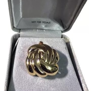 May include: A gold-toned knot-shaped brooch in a gray velvet box with the word "Monet" printed on the lid. The box also has the text "Not for Resale" printed on the inside.