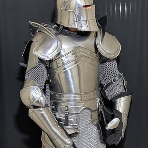 May include: A full suit of polished steel armor, including a helmet with a cross design, shoulder guards, and chainmail. The armor is highly reflective, with visible rivets and articulated joints. The gloves are black.