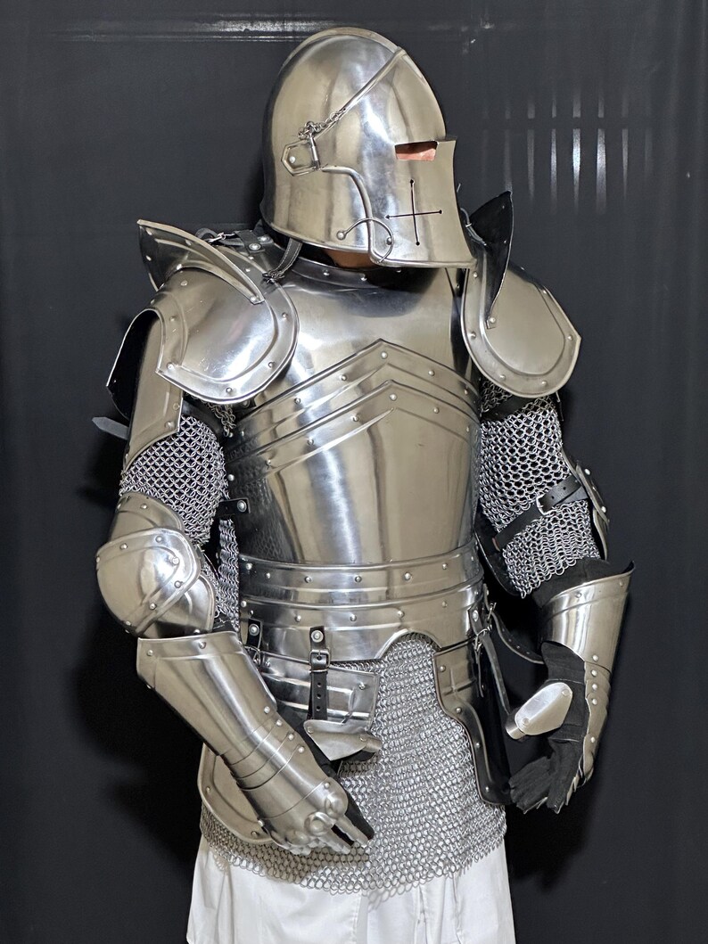 May include: A full suit of polished steel armor, including a helmet with a cross design, shoulder guards, and chainmail. The armor is highly reflective, with visible rivets and articulated joints. The gloves are black.