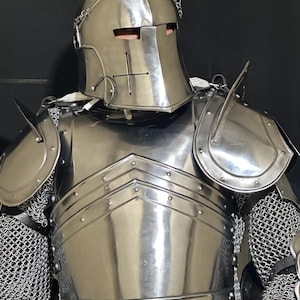 May include: A full suit of polished steel armor, including a helmet with a cross emblem, shoulder guards, and a chest plate. The armor features chainmail at the joints and a reflective surface.