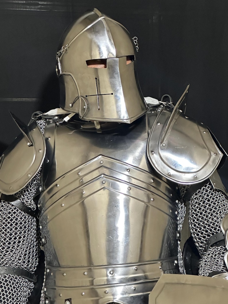 May include: A full suit of polished steel armor, including a helmet with a cross emblem, shoulder guards, and a chest plate. The armor features chainmail at the joints and a reflective surface.