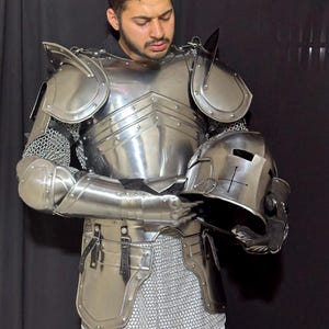 May include: A full suit of polished steel armor, including a breastplate, shoulder guards, arm and leg protection, and a helmet. The armor is connected with chainmail. The helmet is held in the hands.