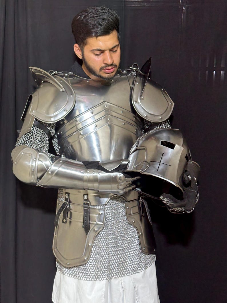 May include: A full suit of polished steel armor, including a breastplate, shoulder guards, arm and leg protection, and a helmet. The armor is connected with chainmail. The helmet is held in the hands.