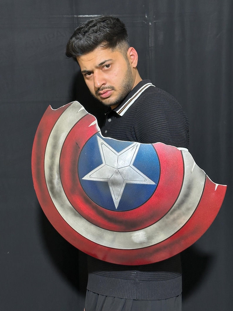 Op de afbeelding: Een Captain America schild prop met een distressed afwerking. Het schild heeft een blauwe centrale cirkel met een witte ster, omringd door rode en witte concentrische ringen. Het schild heeft een gevechtsversleten uiterlijk.