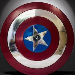 May include: A round shield with a red outer ring, a silver inner ring, and a blue center. A silver five-pointed star is in the center of the blue circle. The shield is a replica of Captain America's shield.