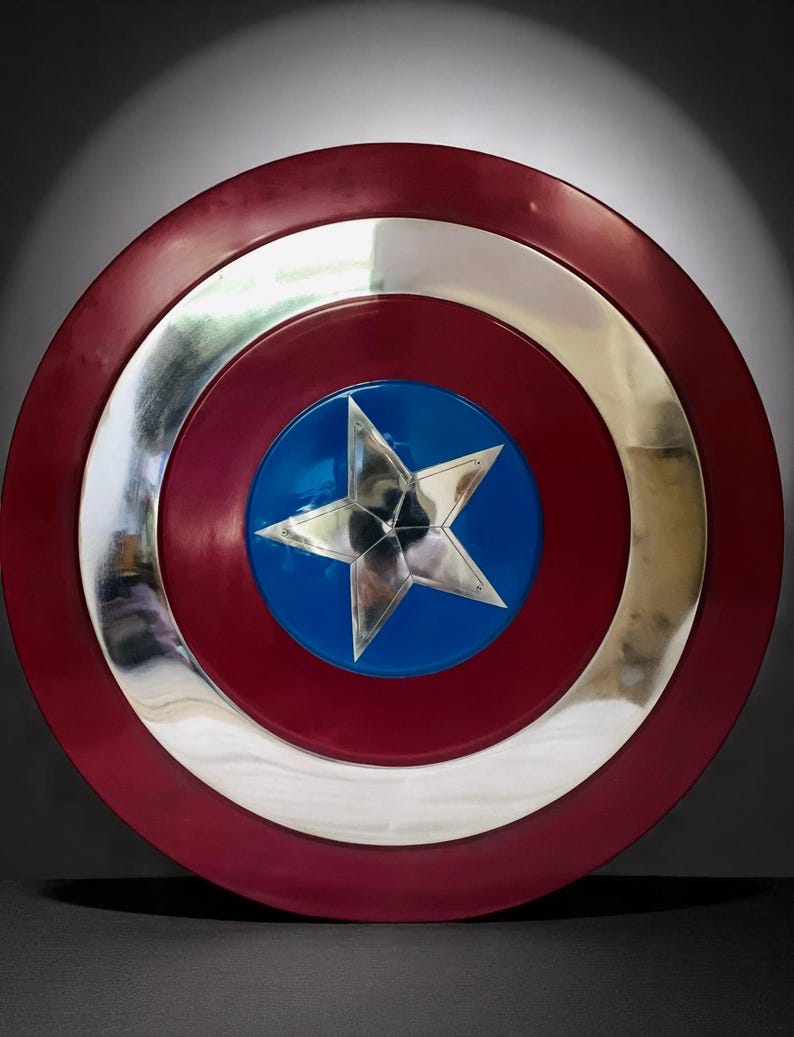May include: A round shield with a red outer ring, a silver inner ring, and a blue center. A silver five-pointed star is in the center of the blue circle. The shield is a replica of Captain America's shield.