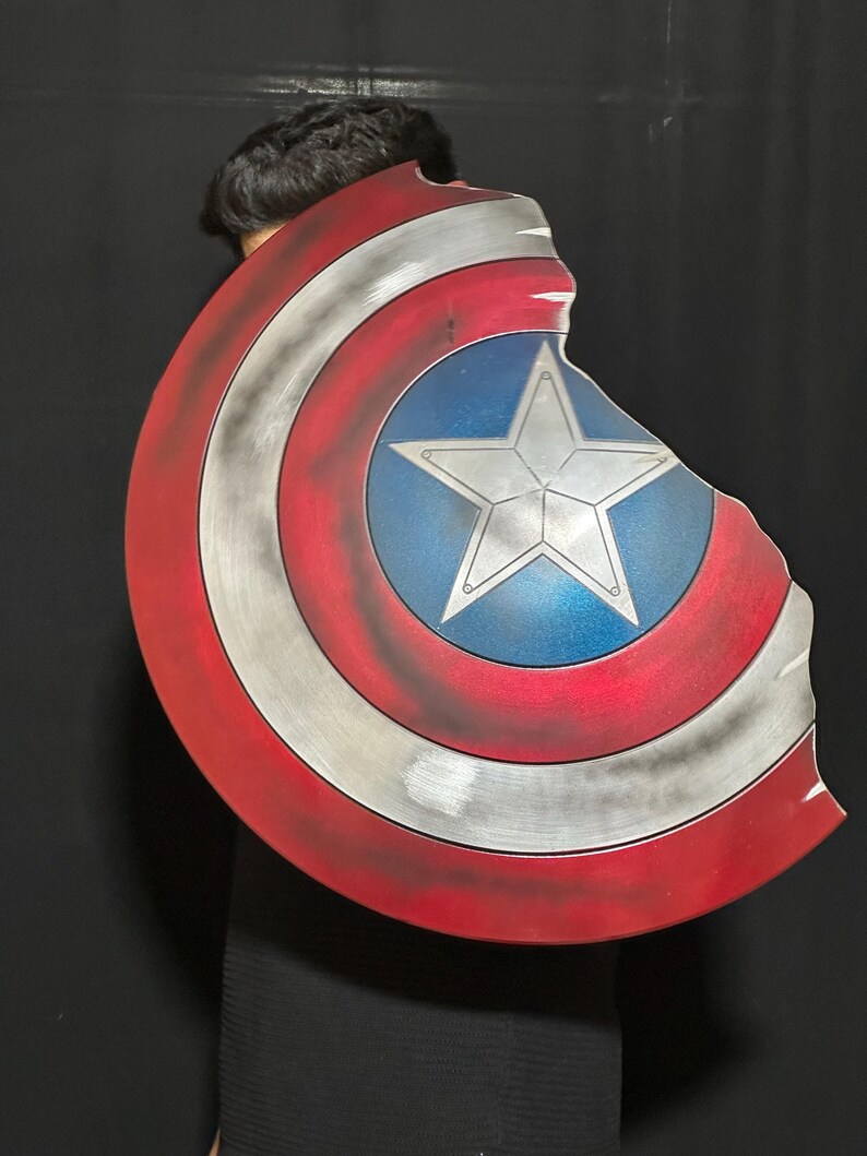 Op de afbeelding: Een Captain America-schild met een distressed design. Het schild heeft een rood-witte gestreepte rand, een zilverkleurig metalen midden en een blauwe ster in het midden. Het schild heeft een gebroken rand.