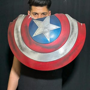 Op de afbeelding: Een Captain America schild rekwisiet, met een rood, wit en blauw kleurenschema. Het schild heeft een centrale blauwe cirkel met een witte ster, een zilveren band en rode buitenranden. Het schild is licht beschadigd.