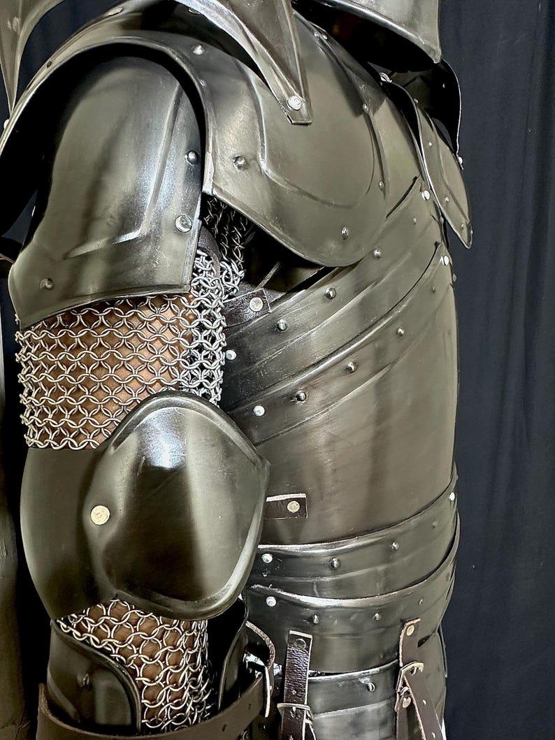 K&ouml;nnte beinhalten: Nahaufnahme eines schwarzen Metall-R&uuml;stungsteils. Die R&uuml;stung weist genietete Platten, Kettenhemden und Lederriemen auf. Die Schulter- und Ellbogensch&uuml;tzer sind gebogen und poliert. Die R&uuml;stung ist f&uuml;r den Schutz und die historische Nachstellung konzipiert.