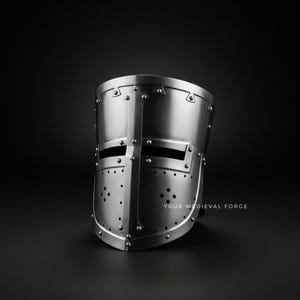 Puede incluir: Casco medieval plateado con construcci&oacute;n remachada. El casco presenta ranuras para los ojos y orificios de ventilaci&oacute;n, con el texto "YOUR MEDIEVAL FORGE" visible en la parte inferior derecha. El casco est&aacute; sobre un fondo oscuro.