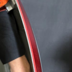 May include: Close-up of a red and silver object with a curved edge. The object has a layered construction, with a red top layer and a silver edge. The background is a dark gray color.