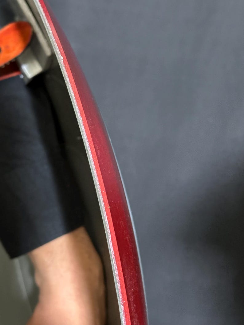May include: Close-up of a red and silver object with a curved edge. The object has a layered construction, with a red top layer and a silver edge. The background is a dark gray color.