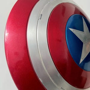 May include: A red, white, and blue Captain America shield. The shield has a metallic red finish with a silver band and a blue circle in the center. A white star is in the center of the blue circle.
