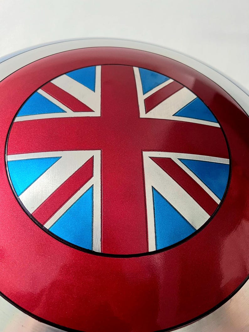 May include: A metallic red shield with a Union Jack design. The shield features a red outer ring, a silver inner ring, and a central design with red, white, and blue elements. The shield is a replica of a superhero's shield.