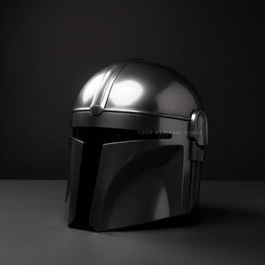 May include: A metallic silver helmet with a visor and a rounded top. The helmet is displayed on a dark gray surface against a black background. The text "YOUR MEDIEVAL FORCE" is visible on the lower right.