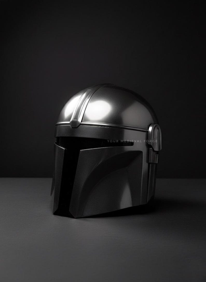 May include: A metallic silver helmet with a visor and a rounded top. The helmet is displayed on a dark gray surface against a black background. The text "YOUR MEDIEVAL FORCE" is visible on the lower right.