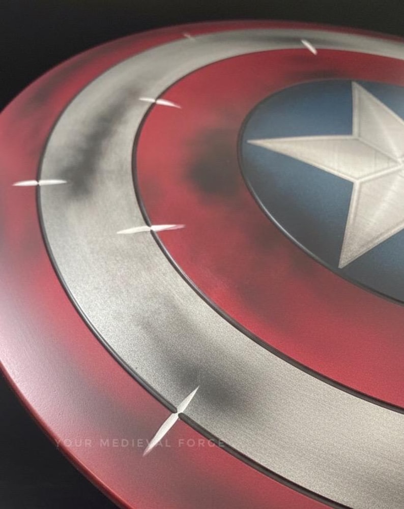 May include: A close-up of a Captain America shield. The shield features a red outer ring, a silver middle ring, and a blue center with a white star. The shield has a distressed look with some dark shading and white accents. The text "YOUR MEDIEVAL FORCE" is visible.