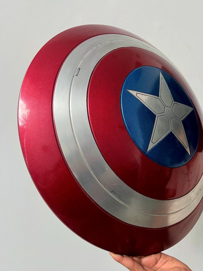 May include: A red, white, and blue Captain America shield. The shield has a metallic finish with a silver ring and a blue center featuring a white star. The shield is a replica of the iconic superhero prop.