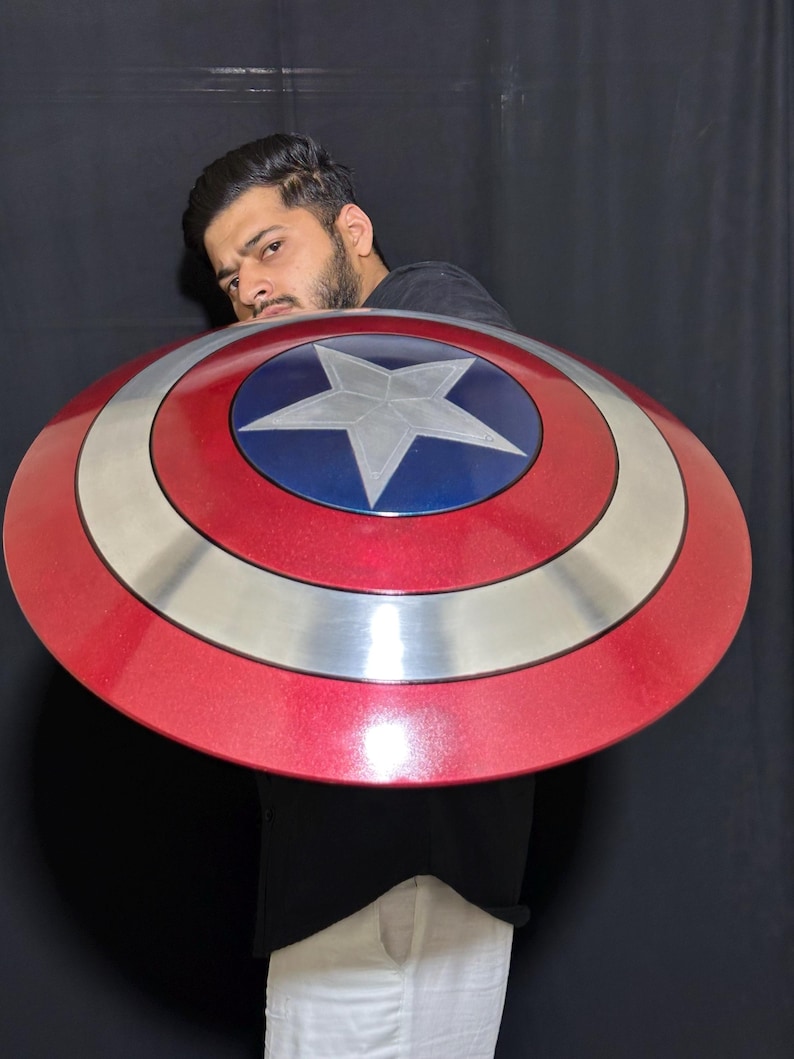May include: A red, white, and blue shield with a star emblem. The shield has a circular design with a silver band separating the red and blue sections. A classic superhero accessory.