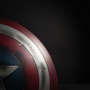 May include: A close-up of a Captain America shield. The shield features a red and white striped design with a silver band and a blue circle with a star in the center. The shield has a distressed, battle-worn appearance.