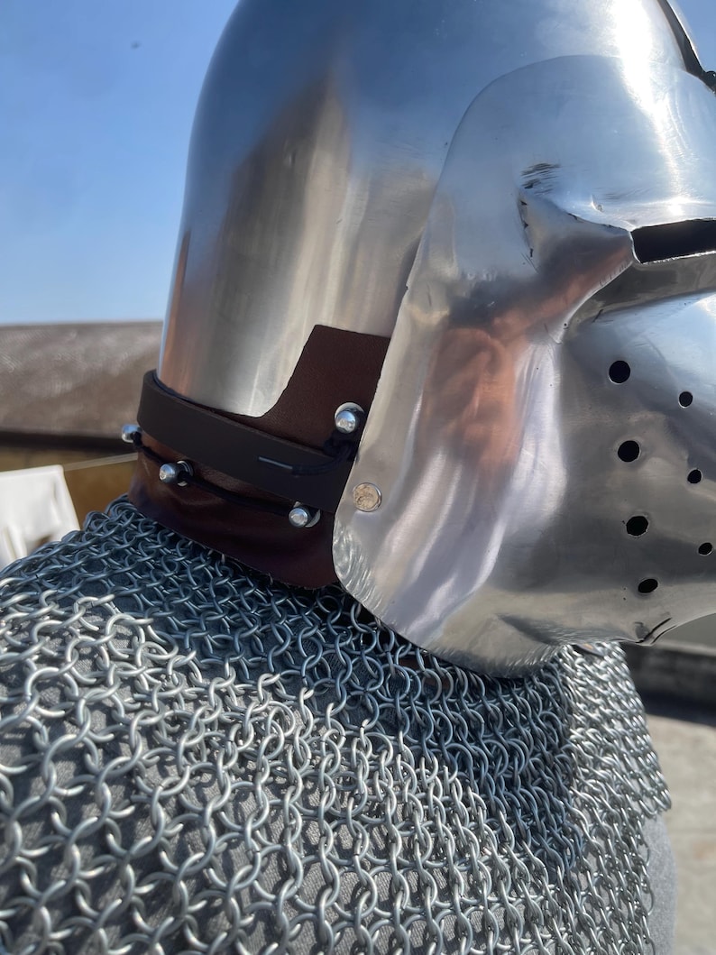 May include: A shiny metal helmet with a visor, brown leather neck guard, and a chainmail shirt. The helmet reflects the light and is secured with rivets. The chainmail is made of interlocking metal rings.