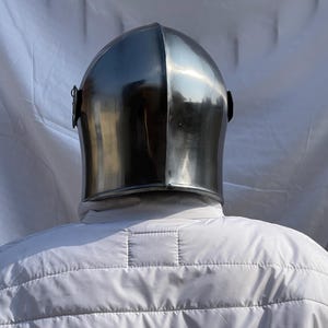 Peut inclure: Un casque en acier poli avec un sommet arrondi et une visi&egrave;re incurv&eacute;e. Le casque est r&eacute;fl&eacute;chissant, montrant l'environnement. Fait partie d'une armure m&eacute;di&eacute;vale.