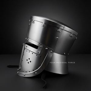 Puede incluir: Un casco medieval pulido de color plateado con una construcci&oacute;n remachada. El casco presenta una visera con m&uacute;ltiples agujeros peque&ntilde;os y una protecci&oacute;n para el cuello. El texto "YOUR MEDIEVAL FORGE" est&aacute; impreso en la parte inferior derecha.