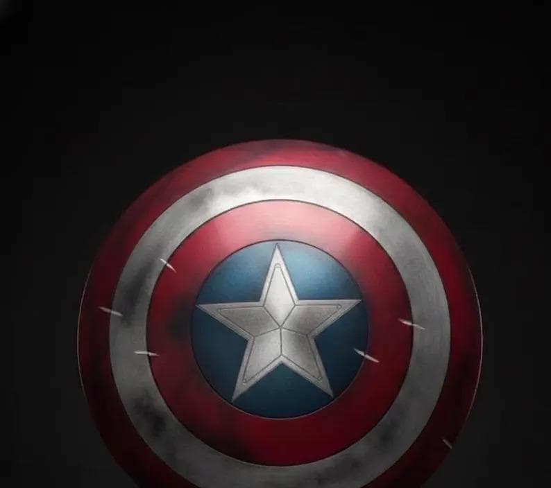 May include: A round shield with a red, white, and blue color scheme. The shield features a white star on a blue circle in the center, surrounded by concentric red and white bands. The shield has a distressed appearance.