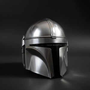 May include: A silver-colored helmet with a sleek, futuristic design. The helmet has a rounded top with a central ridge and a visor area. The text "YOUR MEDIEVAL FOR" is printed on the visor. The helmet is set against a dark background.