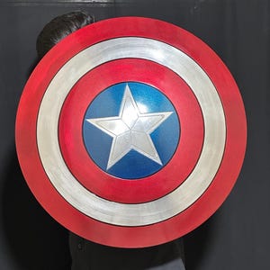 May include: A red, white, and blue shield with a silver star in the center. The shield has a circular design with concentric rings of red, silver, and white. The center is blue with a silver star.
