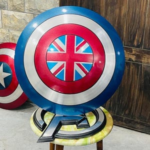 May include: Two round shields with a blue, red, and silver color scheme. One shield features a white star on a red background, while the other has a Union Jack design. The shields are props, possibly for cosplay or display.