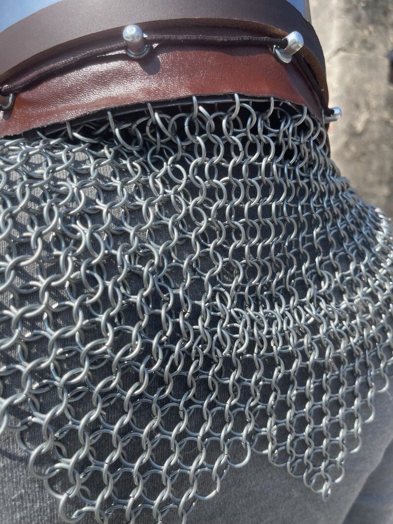 May include: Close-up of a chainmail coif with a brown leather neckband. The chainmail is made of small, interlocking metal rings. The leather neckband is secured with silver rivets.
