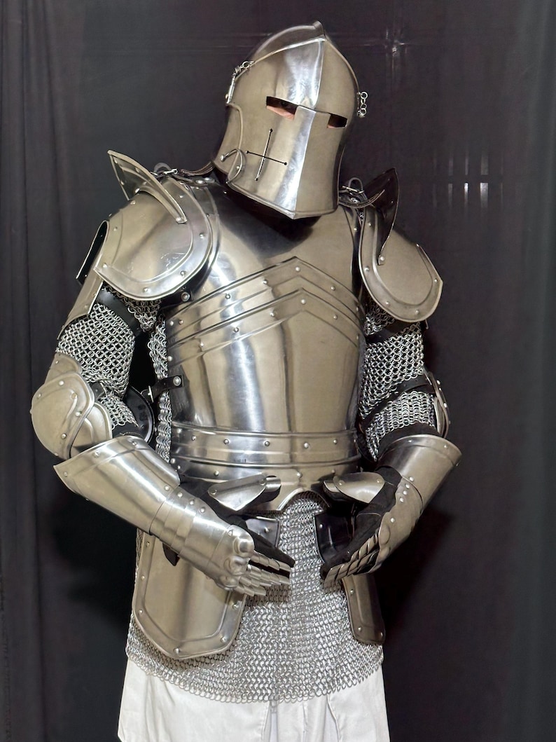 May include: A full suit of medieval armor made of polished steel. The armor includes a helmet with a cross design, shoulder guards, chest and back plates, arm and leg protection, and chainmail. The suit is designed to protect the wearer.