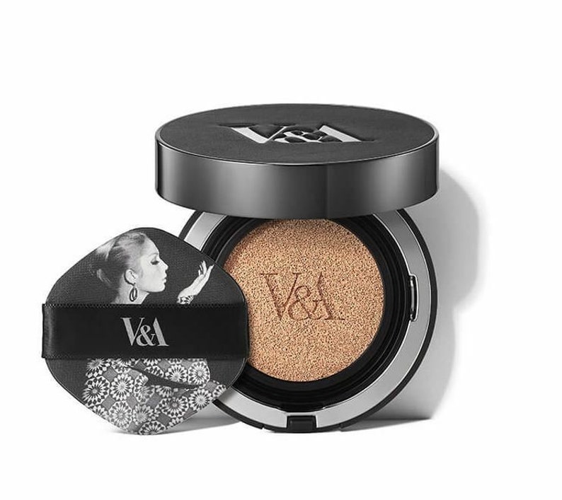 May include: A black and silver compact foundation with a cushion applicator. The compact has a black and white image of a woman with the text "V&A" on the front.