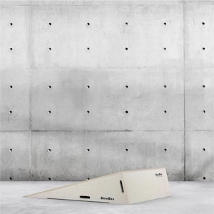Puede incluir: Una rampa de madera con el texto "ShredBox" en el lateral. La rampa está delante de una pared de hormigón con un patrón de agujeros.