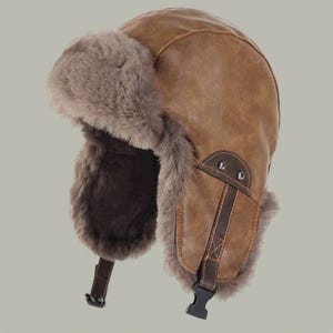 May include: A brown aviator hat with faux fur ear flaps and a leather strap with a buckle. The hat is made of a brown, textured material and has a warm, cosy appearance. The ear flaps are lined with soft, grey faux fur.