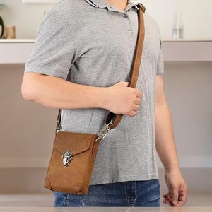 May include: A brown leather crossbody bag with a flap closure and a silver buckle. The bag has a long adjustable strap and is worn by a person.