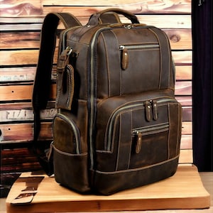 May include: A brown leather backpack with multiple pockets and zippers. The backpack has a distressed look and is made of high-quality leather.