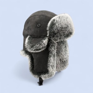 May include: A dark gray trapper hat with faux fur trim. The hat features ear flaps and a button closure on top. The ear flaps are lined with gray faux fur. The hat is designed to provide warmth and protection from the cold.