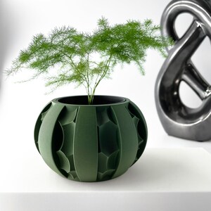 May include: A green, geometric planter with a small plant growing inside. The planter has a round shape with a textured surface.