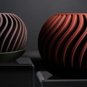 May include: Two spherical decorative objects. One is a dark brown colour, and the other is a reddish-orange colour. Both have a spiral design and sit on a dark base. The objects are likely for home decor.