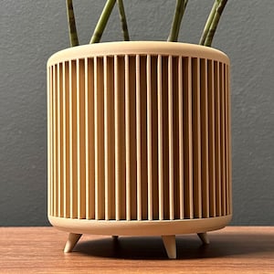 May include: A light brown wooden planter with vertical slats and three short legs. The planter is empty.