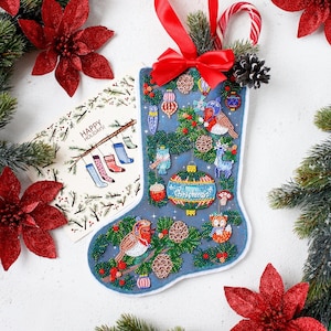 Puede incluir: Un calcetín navideño azul con adornos de cuentas de pájaros, adornos y un ciervo. El calcetín está decorado con un lazo rojo, un bastón de caramelo y una ramita de pino. También hay una tarjeta con el texto "HAPPY HOLIDAYS!".