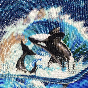 May include: A detailed beadwork tapestry featuring two orcas swimming in a turbulent ocean. The scene displays black and white orcas amidst swirling blue, white, and tan waves, with green seaweed accents, all crafted from tiny, uniform glass beads.