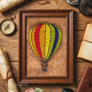 May include: A framed string art piece depicts a colorful hot air balloon against a wood-grain background. The balloon features vibrant bands of red, yellow, green, and blue. The frame is a dark brown, and the artwork is surrounded by vintage travel-themed items.